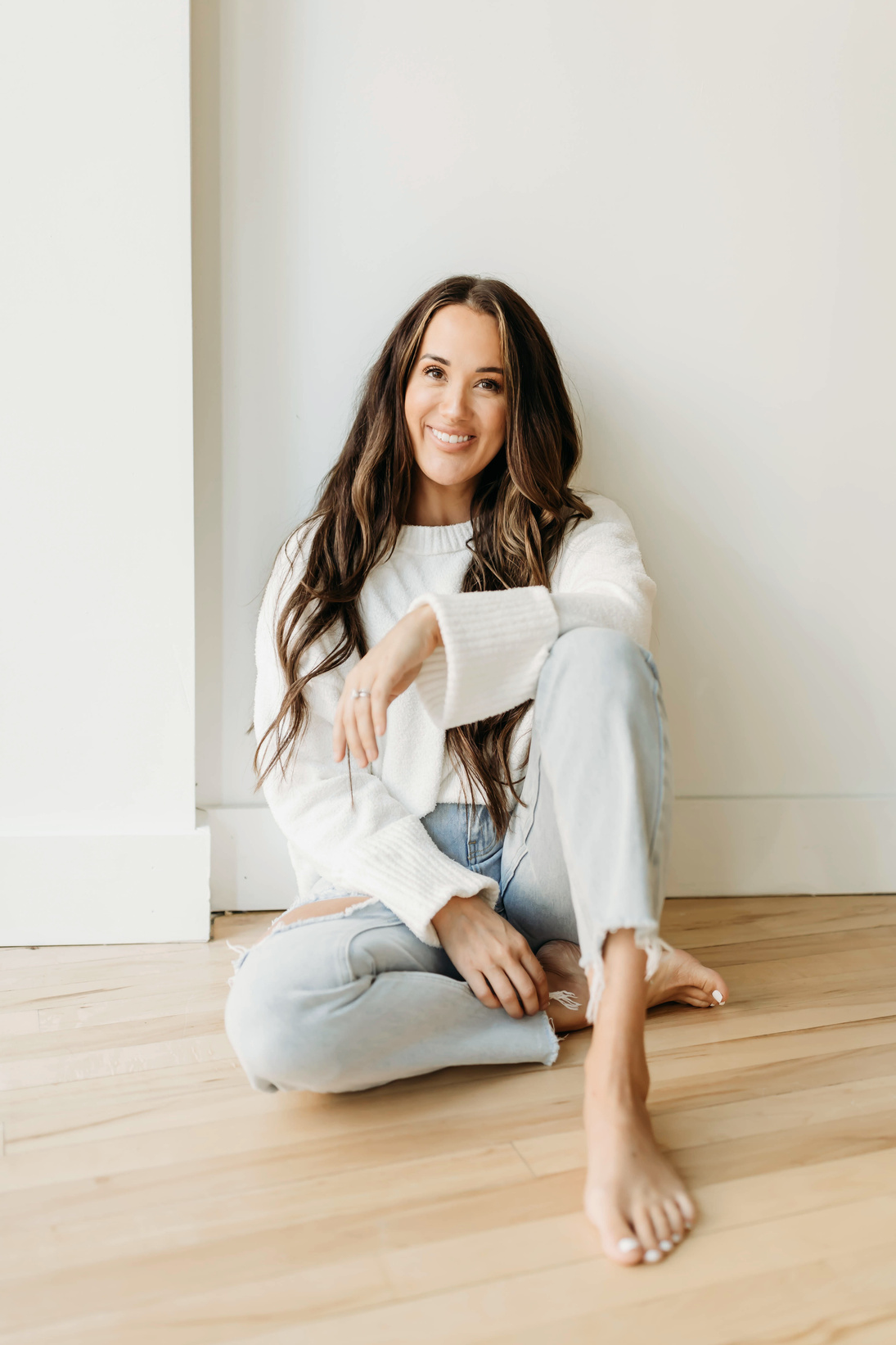 a person sitting on the floor wearing jeans and a white sweater